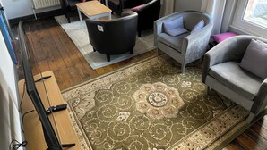 A living room with a large patterned rug, two black armchairs, a grey sofa, and a wooden coffee table.