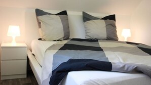 Un lit bien fait, avec une couvre-lit à rayures et deux oreillers, une table de chevet avec une lampe et un plancher en bois.