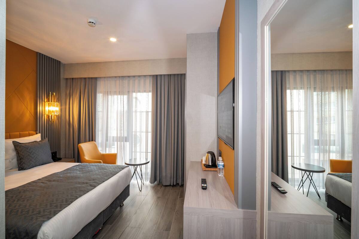 A hotel room with a large bed, a sofa, a TV, a coffee maker, and a small table.