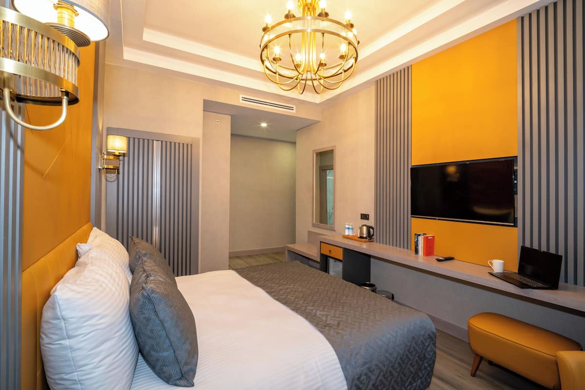 A hotel room with a large bed, a desk with a TV, a chandelier, and a mirror.