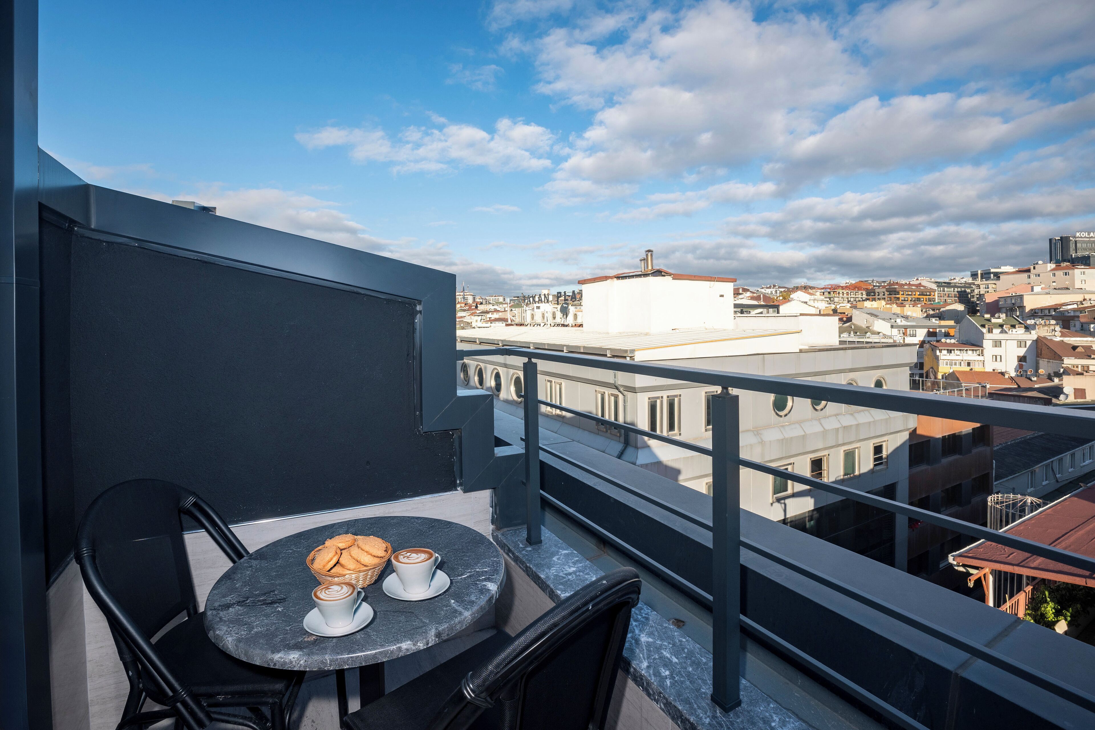 A balcony with a table set for two, a chair, and a view of the cityscape.