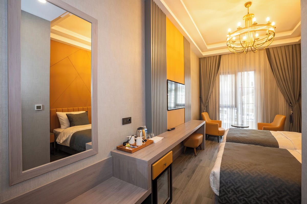 A hotel room with a large mirror, a desk with a tray of items, two beds, a chandelier, and a TV.