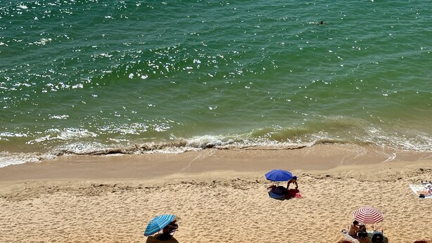 Une plage de sable avec deux parasols et une personne allongée sur le sable.