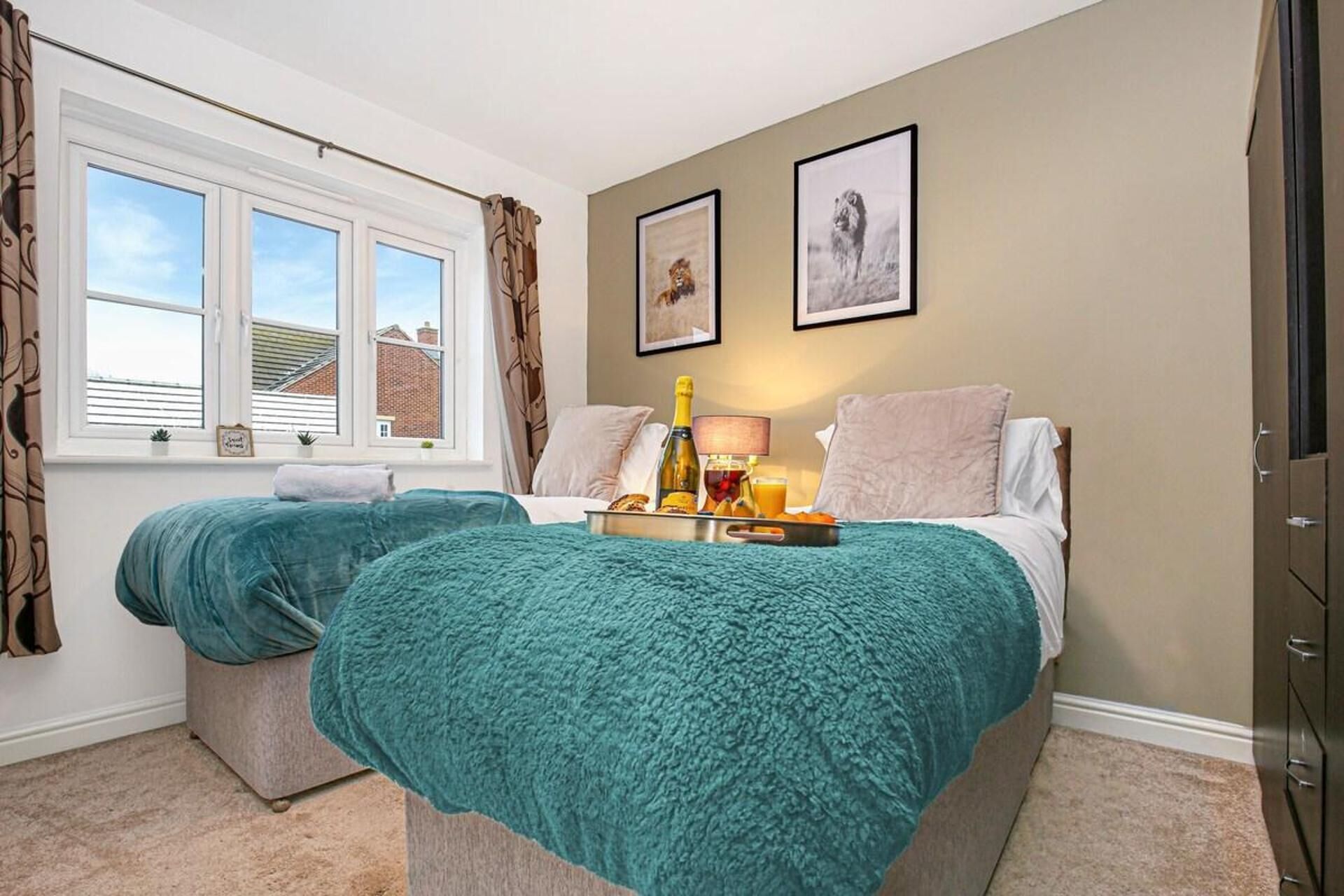 A hotel room with two beds, a window with curtains, a tray with breakfast items, and two framed pictures on the wall.