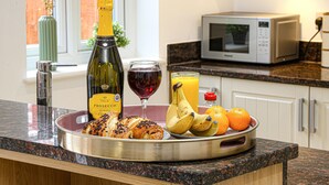 Ein Frühstücksbrett mit Croissants, Bananen, Orangen, einer Prosecco-Flasche und einem Glas Rotwein auf einer Küchenarbeitsplatte.
