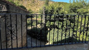 Balcó de pedra amb barana de ferro forjat amb vista a un turó ple d'arbres i un cel blau clar.