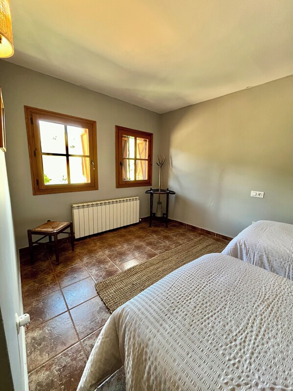 A room with two beds, a radiator, a window, and a small table.