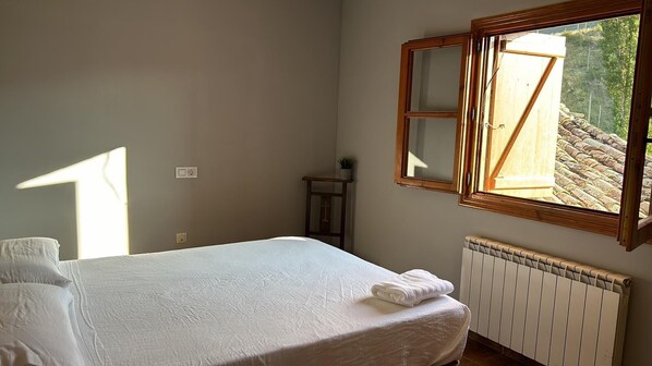 A bedroom with a bed, a radiator, a window, and a small table.
