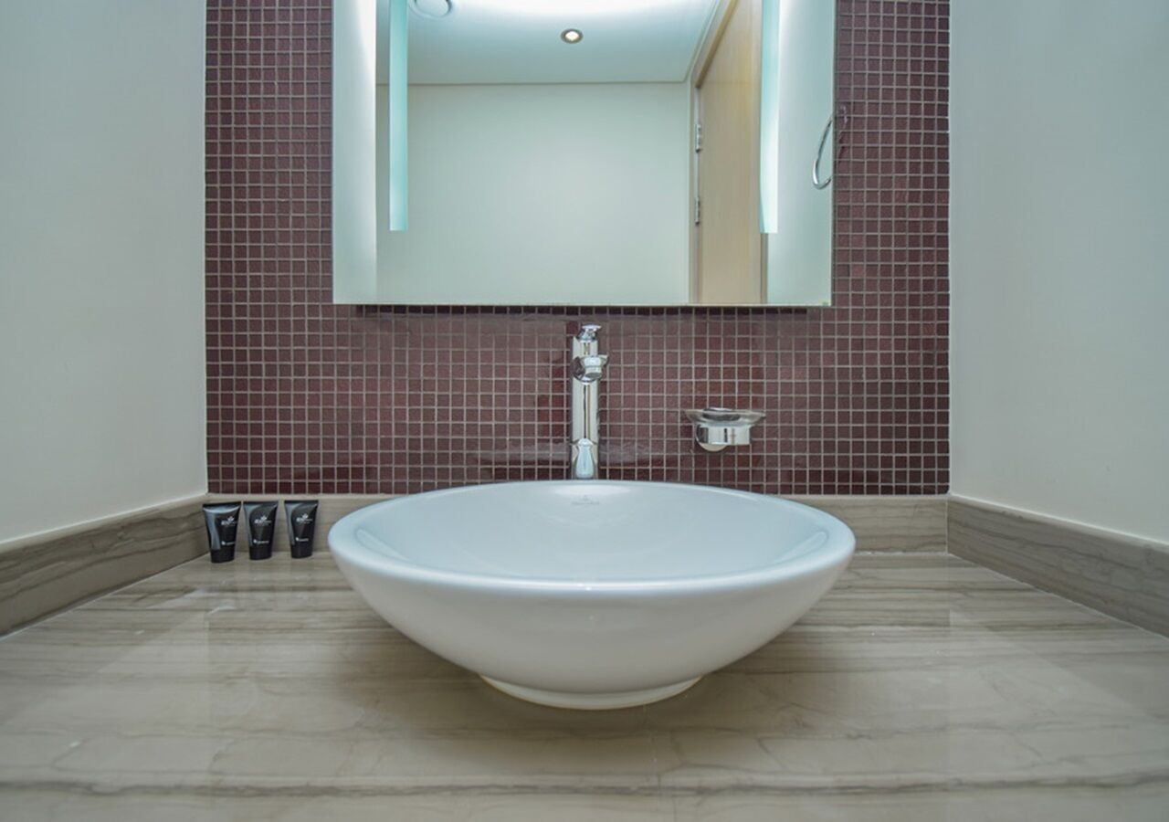 A bathroom with a large white sink, a mirror above it, and red-tiled walls.