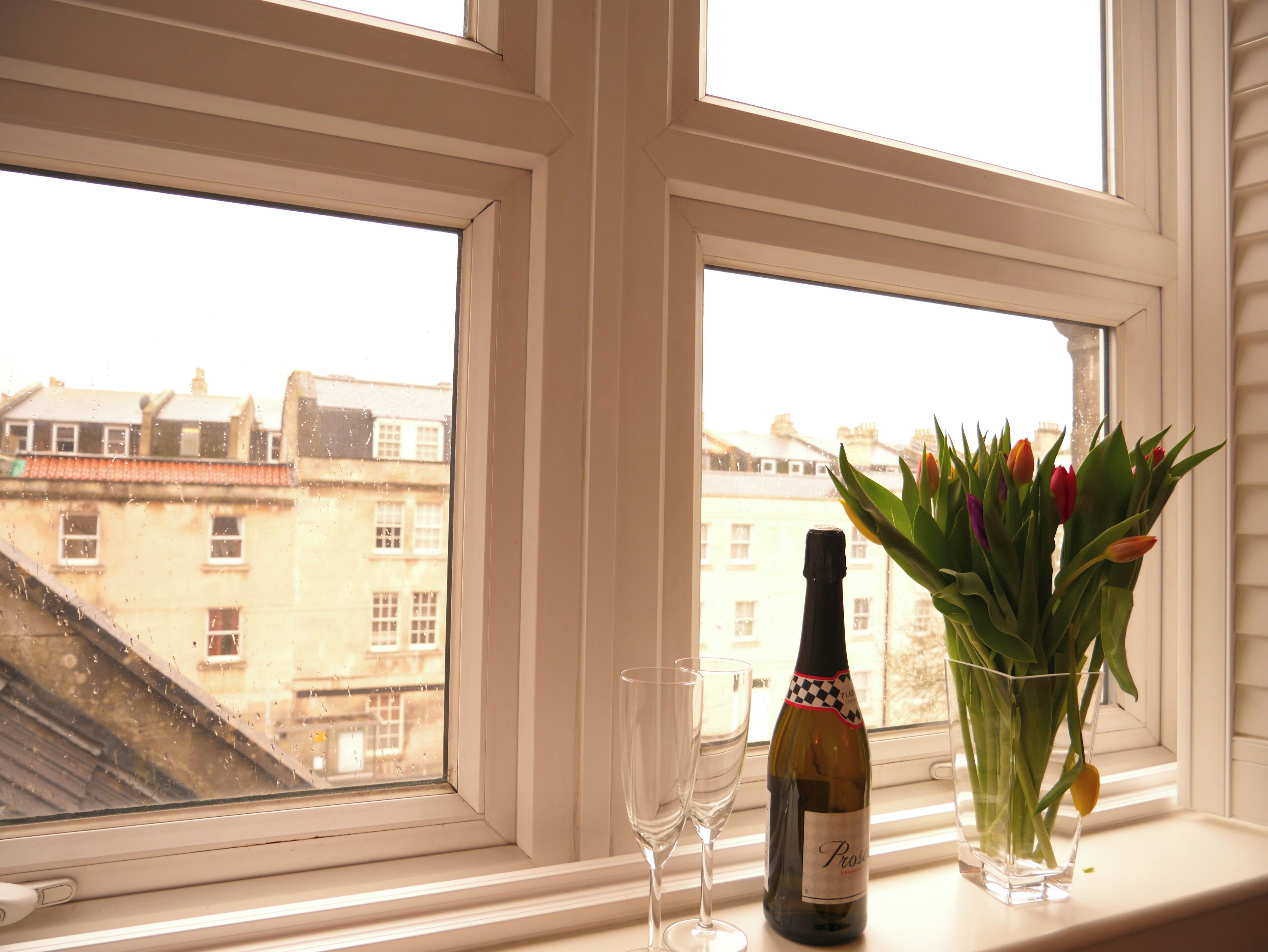 A window with a bottle of wine and a vase of tulips on a windowsill.