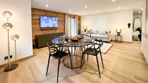 A modern living room with a dining area, a TV mounted on a wooden wall, and a white sofa. - Sapins302 | 2024 Apt | Near center & slopes (Les Gets)