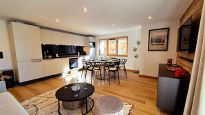 A modern kitchen with white cabinets and a dining area with a round table and chairs. - Sapins302 | 2024 Apt | Near center & slopes (Les Gets)