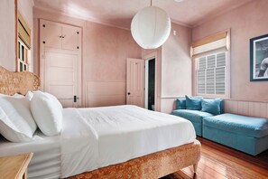 Une chambre avec un lit, un canapé bleu, un plancher en bois et une porte blanche.