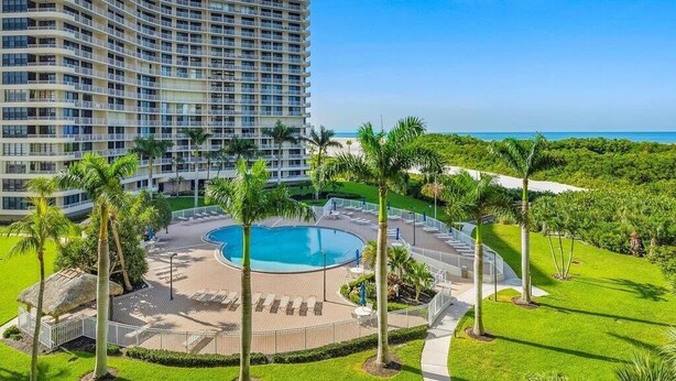 A hotel with a large pool, palm trees, and a view of the ocean. - Beachfront 2BR condo with pool, WiFi, and heated pool on Marco Island. (Marco Island)