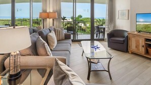 A modern hotel room with a large balcony, a sofa, a coffee table, a TV, and a lamp. - Beachfront 2BR condo with pool, WiFi, and heated pool on Marco Island. (Marco Island)