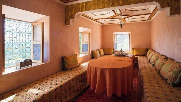 A room with a large round table, a sofa, and two windows with decorative grills. - Ighrem Le Grenier (Tabant)