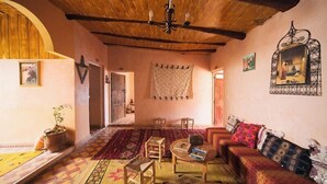 A cozy living room with a wooden ceiling, a patterned rug, a sofa with cushions, and a small table with books. - Ighrem Le Grenier (Tabant)