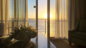 Ein Zimmer mit Meerblick bei Sonnenuntergang, ein grüner Sessel und eine Pflanze auf einem Tisch.