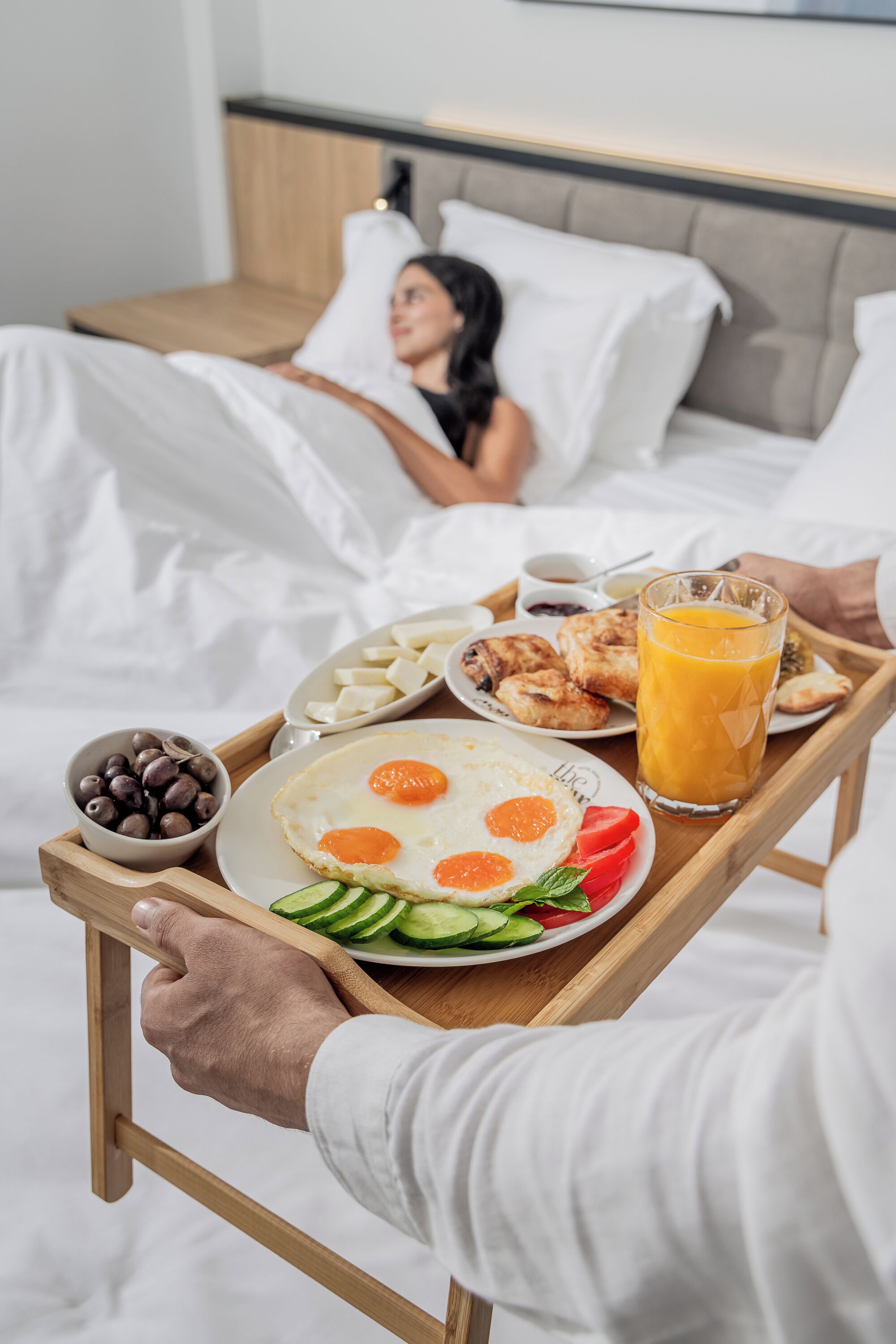 Bandeja de desayuno con huevos, tostadas y jugo, sostenida por una persona en una habitación de hotel.