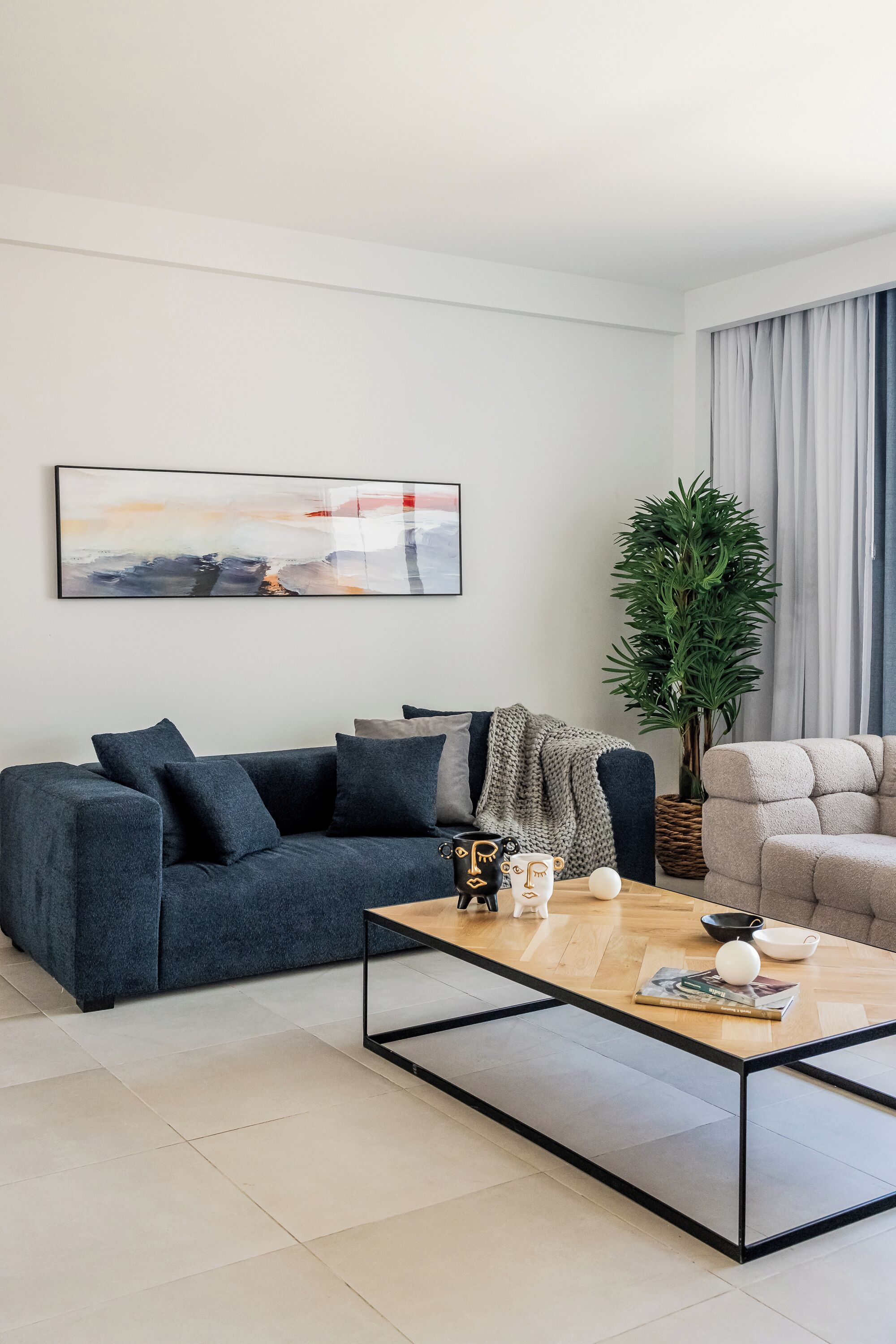 A modern living room with a dark grey sofa, a wooden coffee table, and a large abstract painting on the wall.