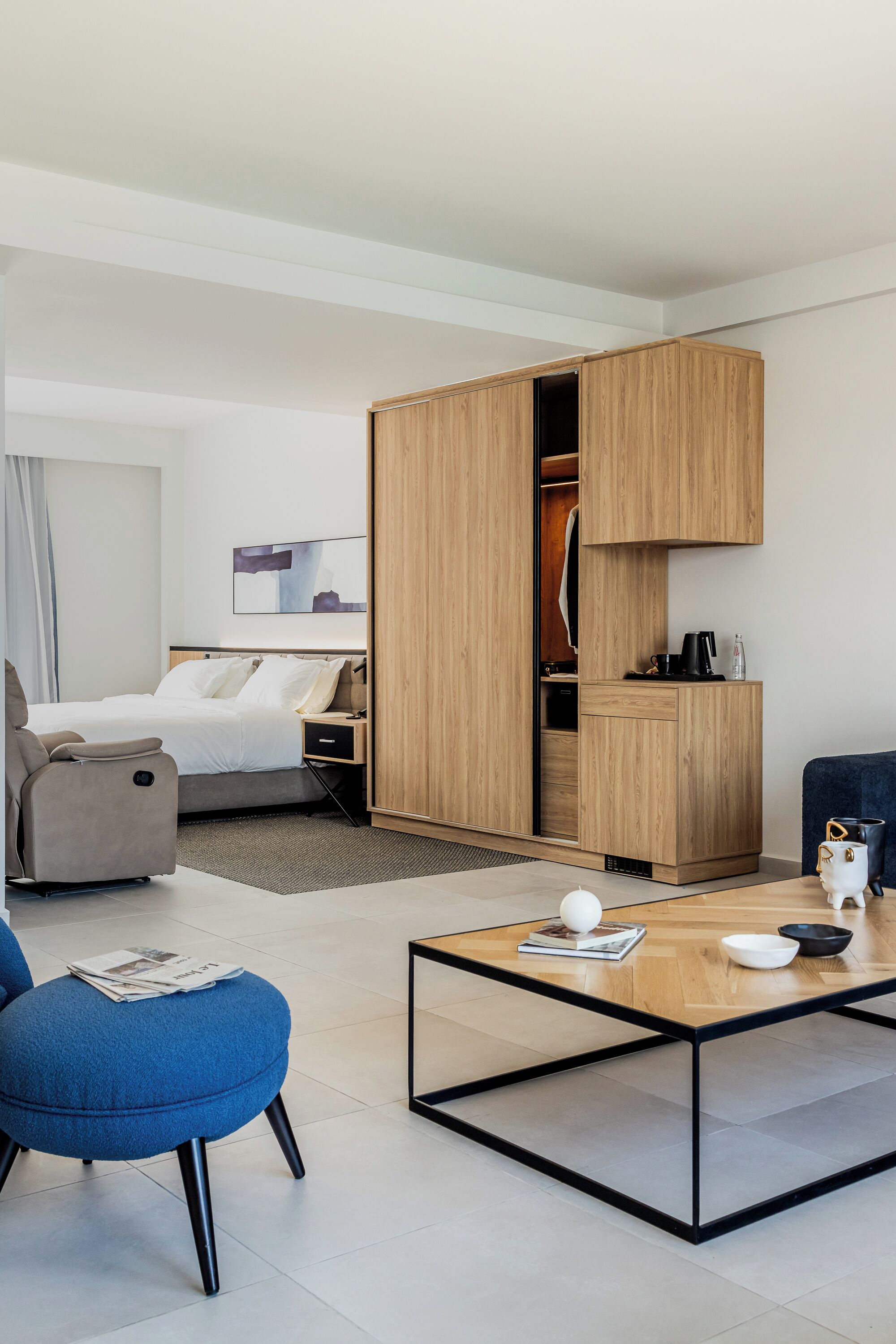Ett modernt hotellrum med en säng, en garderob, en sittgrupp med ett soffbord och ett litet bord med en kopp och en bok.