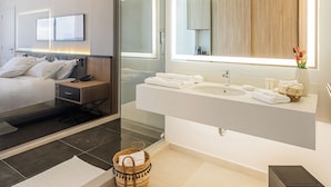 A modern bathroom with a large mirror, a wooden vanity, and a bed with a nightstand. - The View - Saint Georges Hotel (Beirut)