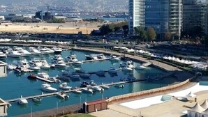 A marina with numerous boats, a swimming pool, and a tall building in the background. - The View - Saint Georges Hotel (Beirut)