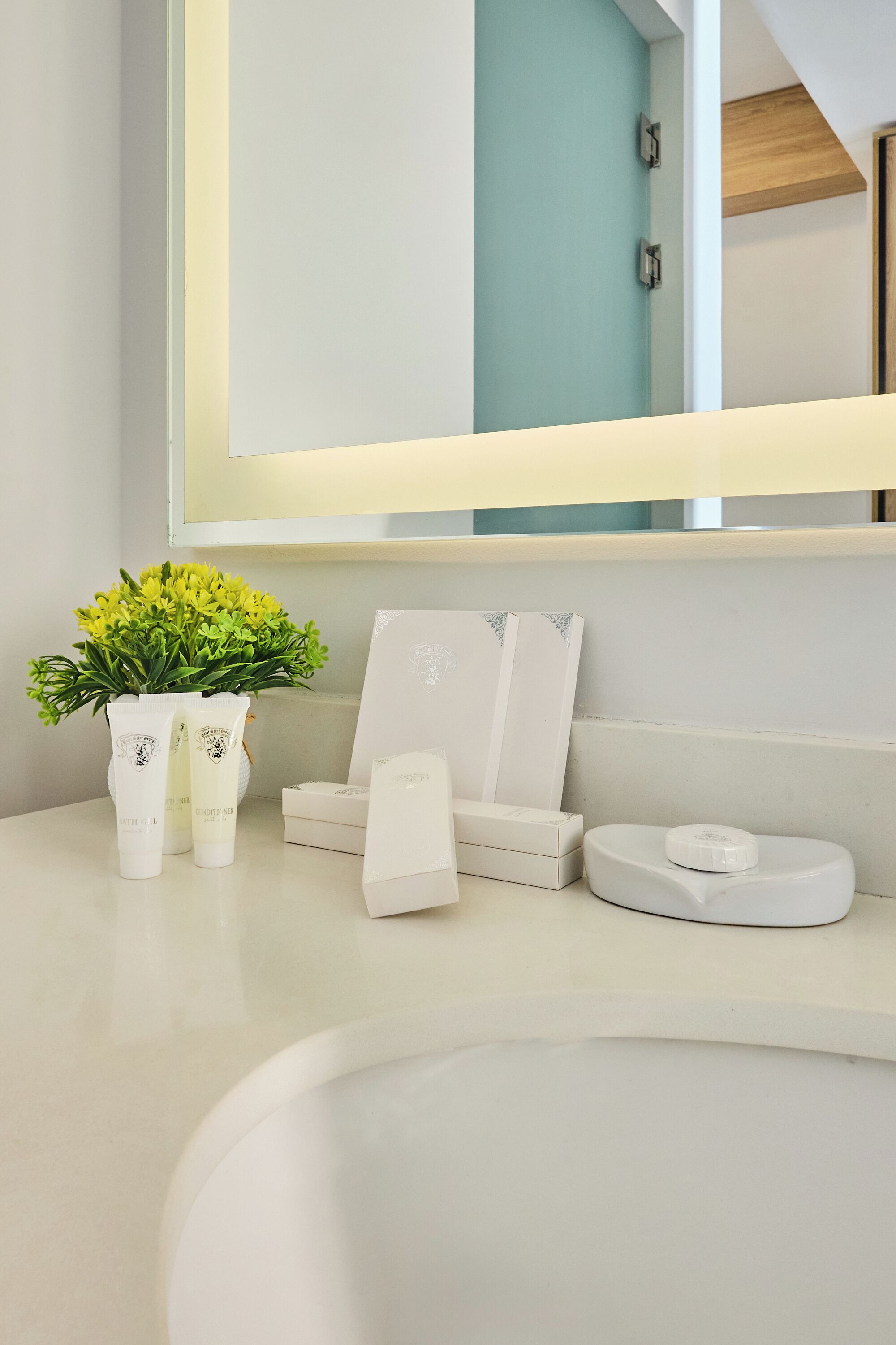 A bathroom vanity with a mirror, a potted plant, a soap dispenser, and a toothbrush holder.