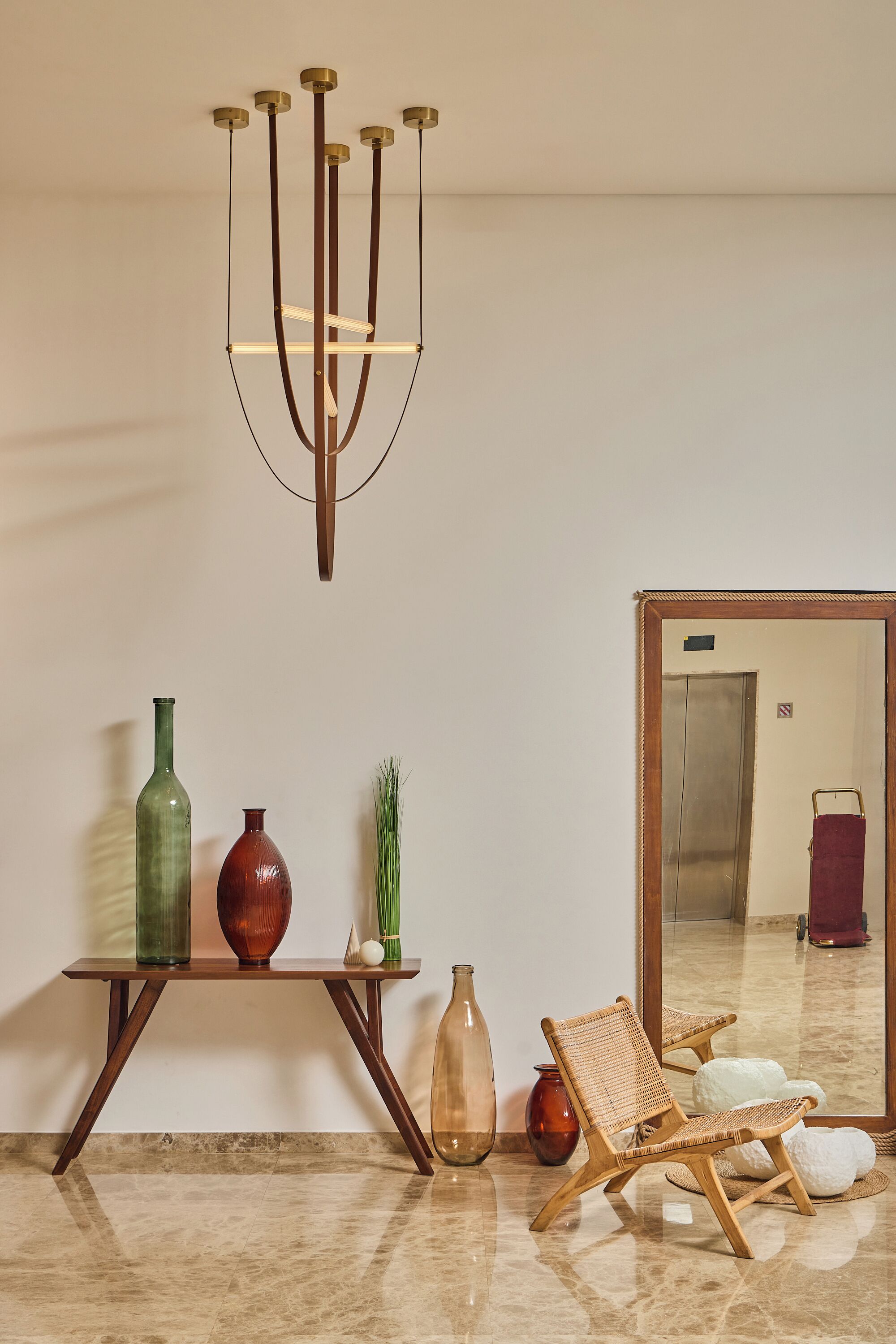 Una stanza con un tavolino consolle in legno, due vasi, una sedia in vimini, uno specchio e un lampadario moderno.