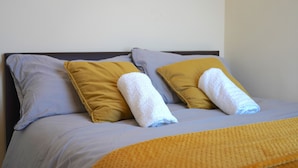 Ein Bett mit zwei Kissen, eines gelb und eines grau, sowie zwei gerollte Handtücher.