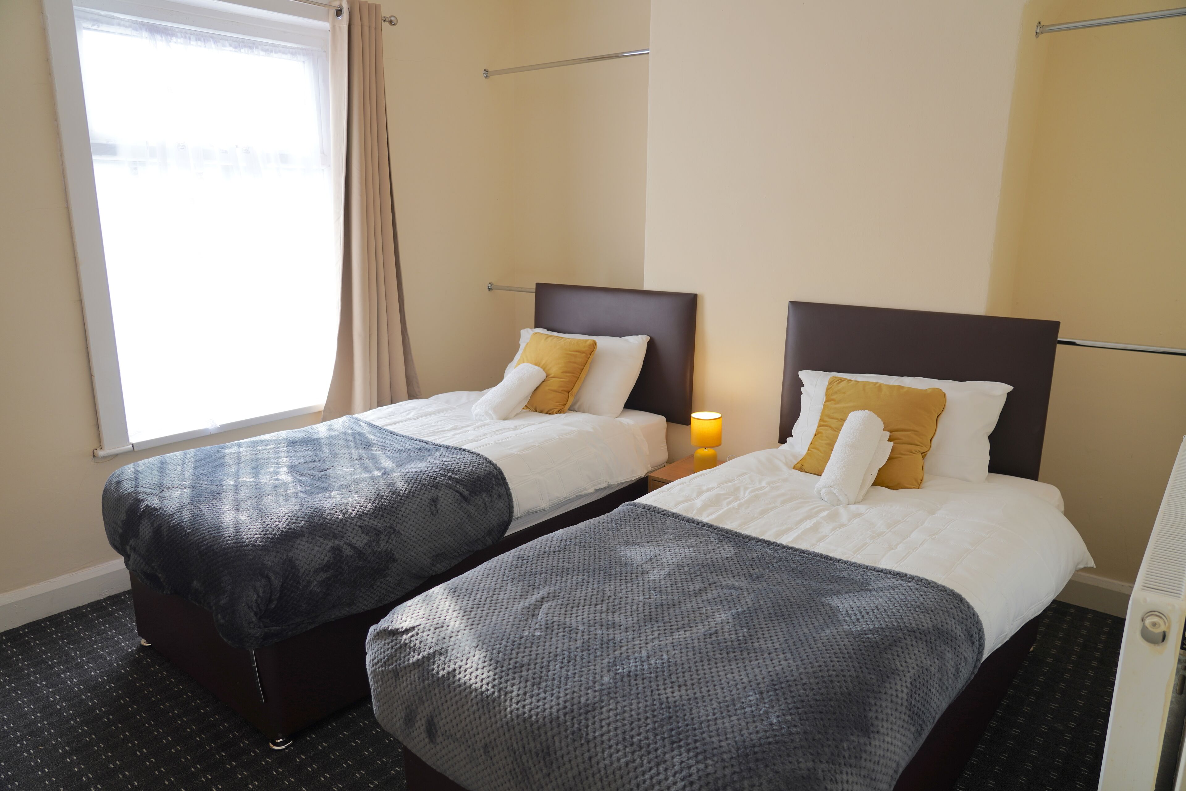 Een hotelkamer met twee bedden, elk met hoofdeinde, een raam met gordijnen en een bedlampje.
