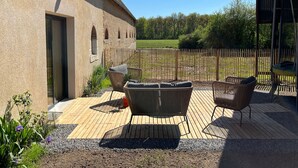 A patio with outdoor furniture, a wooden deck, and a rustic building with arched windows. - Two Berry houses with private garden and shared courtyard, perfect for groups (Thenay)