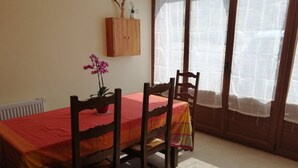 A dining area with a table set for four, wooden chairs, a red tablecloth, a potted plant, and a wooden cabinet against the wall.