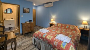 A bedroom with a bed, two bedside lamps, a wooden dresser, a mirror, and a door.