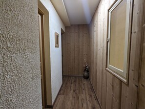 A narrow hallway with wooden walls and a wooden floor. There is a door on the right and a textured wall on the left. - Air-conditioned room with private bathroom, garden access (Rehaupal)