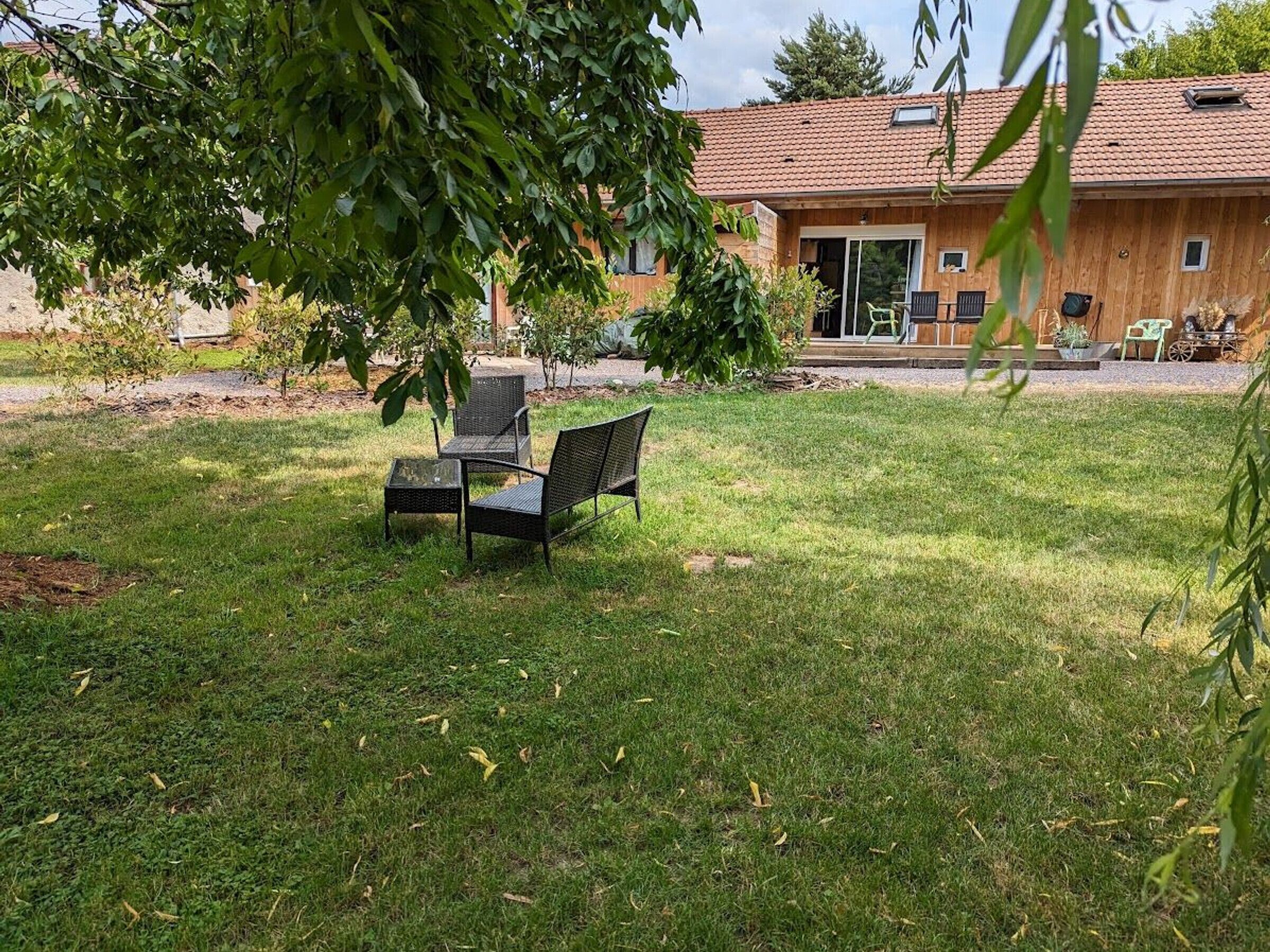 A wooden house with a tiled roof, a covered patio area, and a grassy lawn with outdoor furniture.