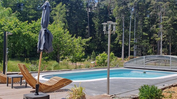 A swimming pool with a wooden deck, lounge chairs, and a covered umbrella.