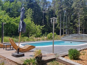 A swimming pool with a wooden deck, lounge chairs, and a covered umbrella. - Peaceful cottage with pool, terrace, and Wifi in the forest for 4 guests (Saint-Remy)