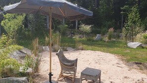 A covered outdoor seating area with a wicker chair and a small table, surrounded by natural scenery and rocks.