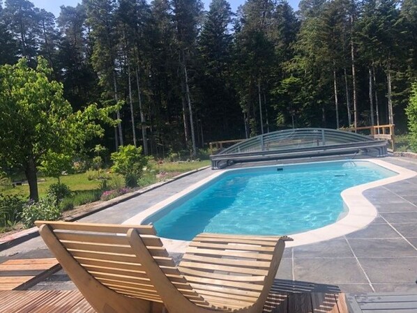 A swimming pool with a wooden deck and lounge chairs, surrounded by a forest. - Peaceful cottage with pool, terrace, and Wifi in the forest for 4 guests (Saint-Remy)