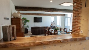Un interior rústico con paredes de ladrillo visto, una barra de madera, un sofá y una zona de comedor con sillas.