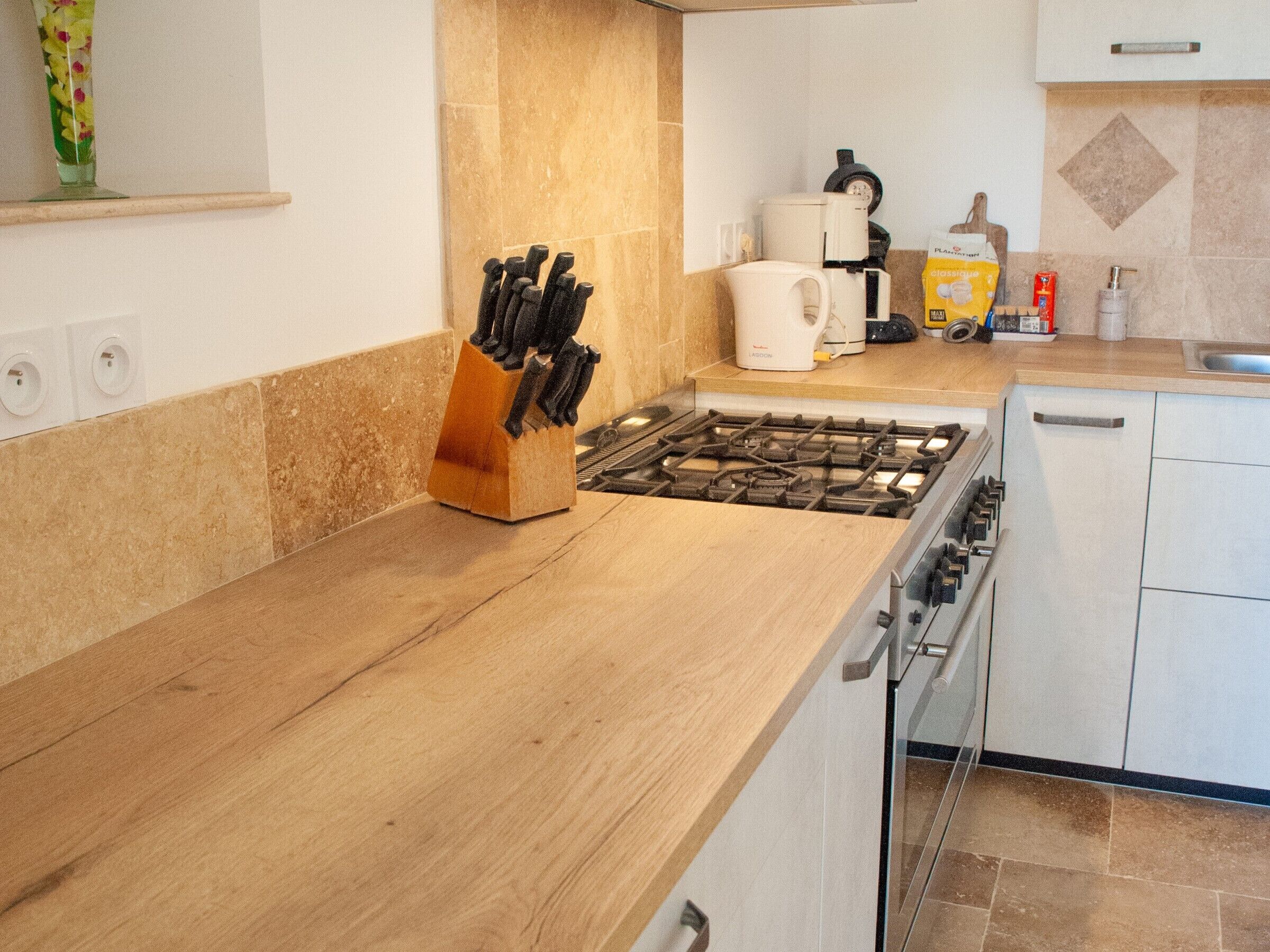 Une cuisine moderne équipée d’une cuisinière à gaz, d’un plan de travail en bois et d’un bloc à couteaux.