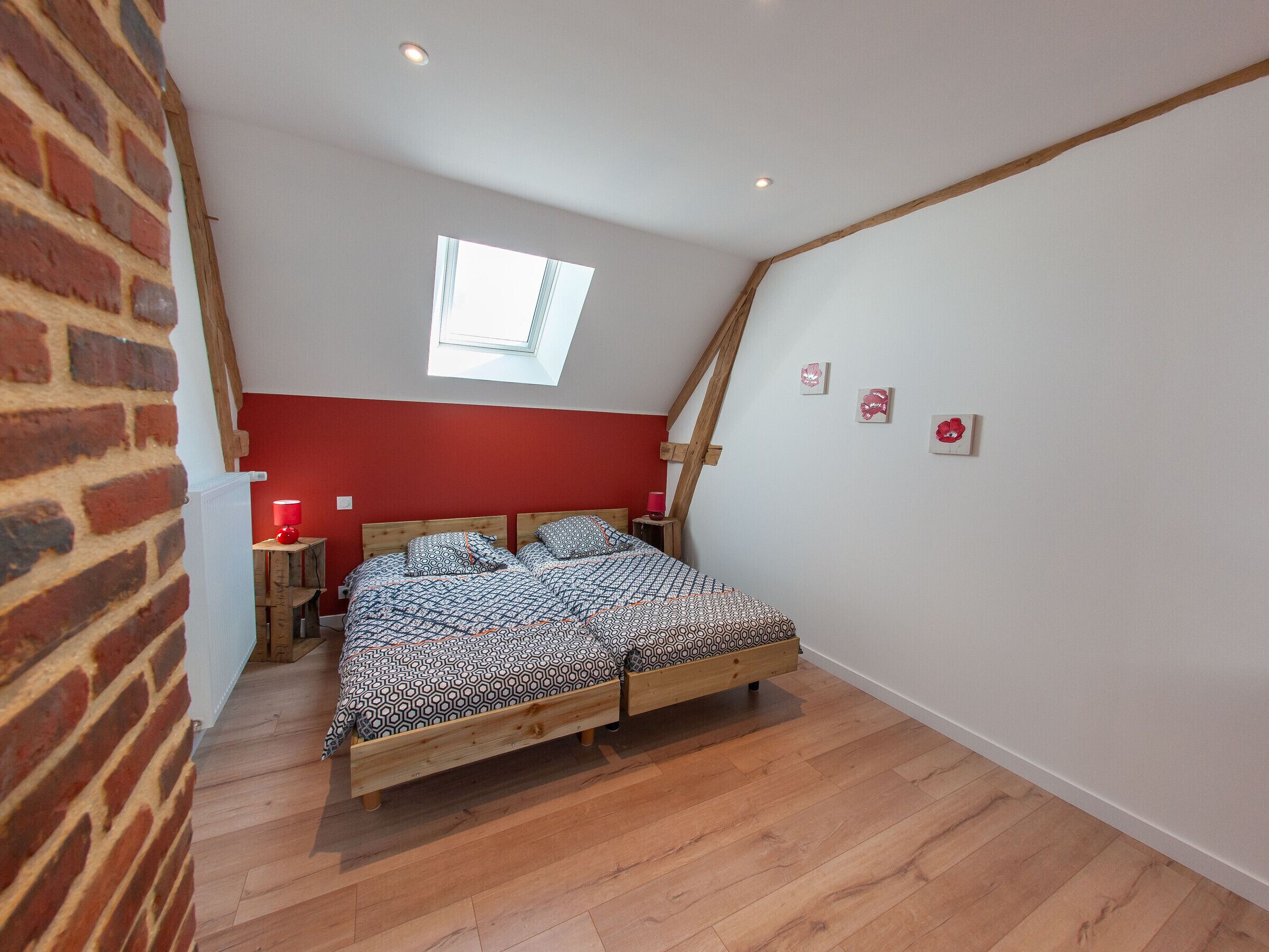 Une chambre avec un plafond en pente, un puits de lumière, un lit en bois et un mur en briques.