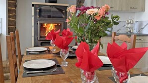 A dining table set with plates, cutlery, and red napkins in glass vases, with a wood-burning stove in the background. - Charming renovated house in Domfront, pets allowed, wifi, near cycling routes (Domfront en Poiraie)