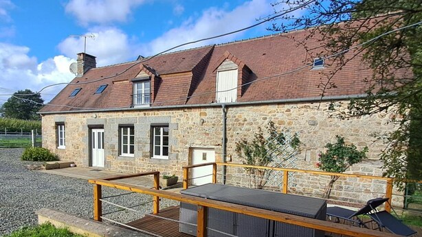 A stone building with a sloped roof, a wooden deck with chairs, and a gravel driveway. - Charming renovated house in Domfront, pets allowed, wifi, near cycling routes (Domfront en Poiraie)
