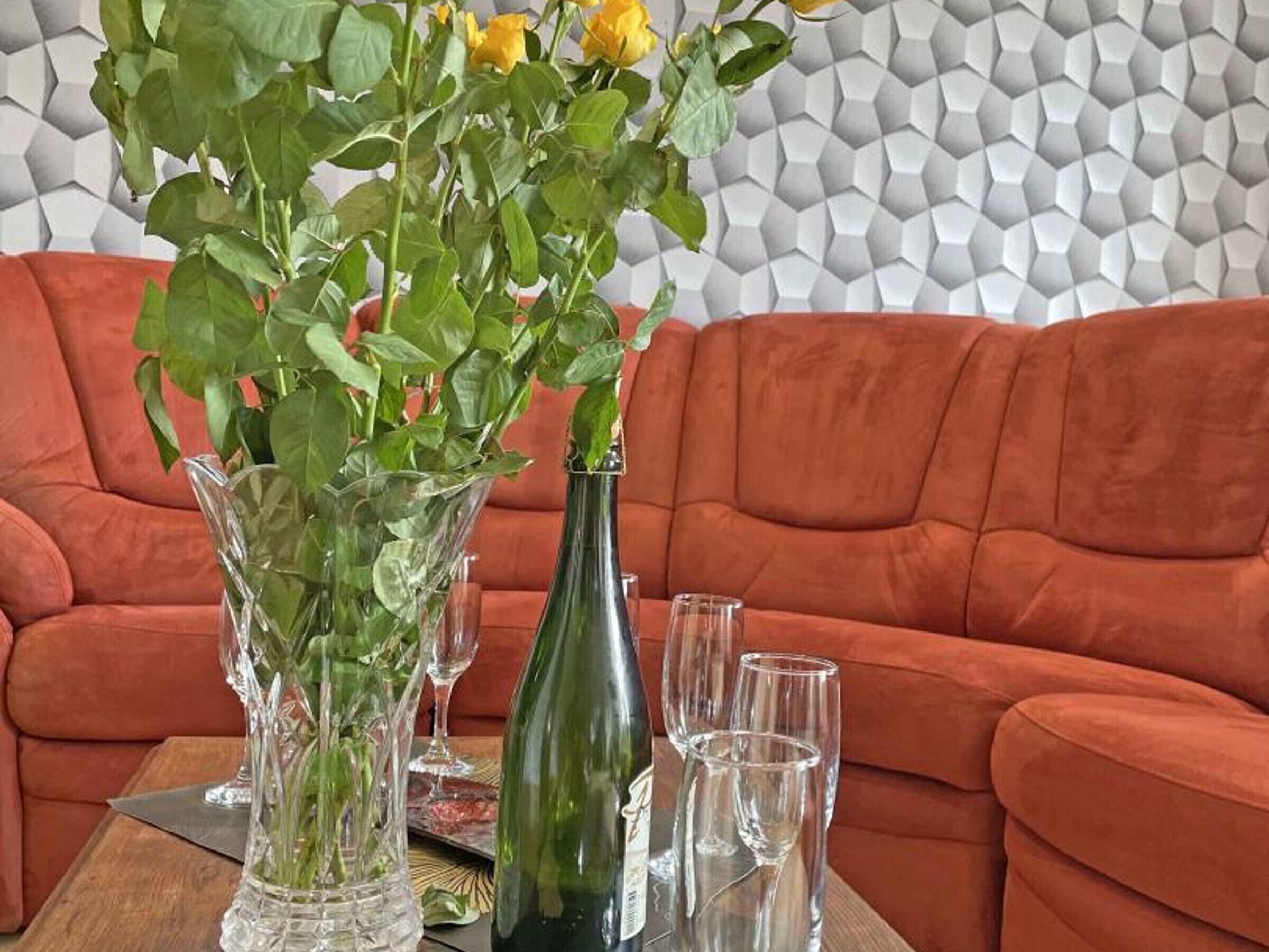 A living room with a sofa, a table with a vase of flowers, a bottle, and glasses.