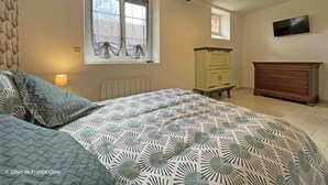 A bedroom with a bed, a dresser, a cabinet, a window with curtains, a TV on the wall, and a wooden beam ceiling. - Charming renovated house in Domfront, pets allowed, wifi, near cycling routes (Domfront en Poiraie)