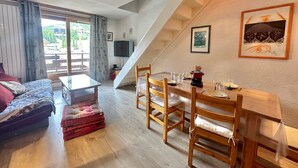 Un salon chaleureux avec un canapé, une table à manger dressée pour deux personnes et un escalier menant à l’étage supérieur.
