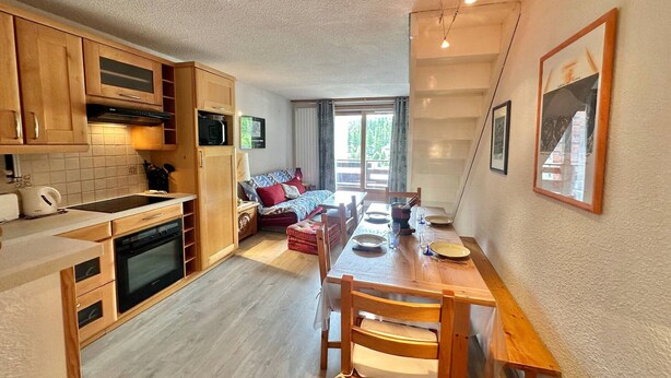 Une cuisine compacte avec des meubles en bois, un coin repas avec une table et des chaises en bois, et un salon avec un canapé et un téléviseur.