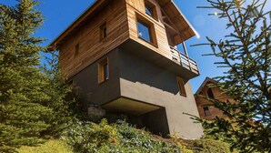 Une cabane moderne en bois, dotée d’un balcon et entourée d’arbres.